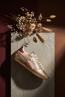 Gold and pink sneaker on a textured surface with dried flowers.