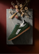 Green sneaker with brown sole on a dark surface with dried flowers